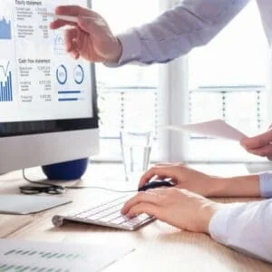 Close-up of two people at a desk, looking at a computer screen, one helping the other