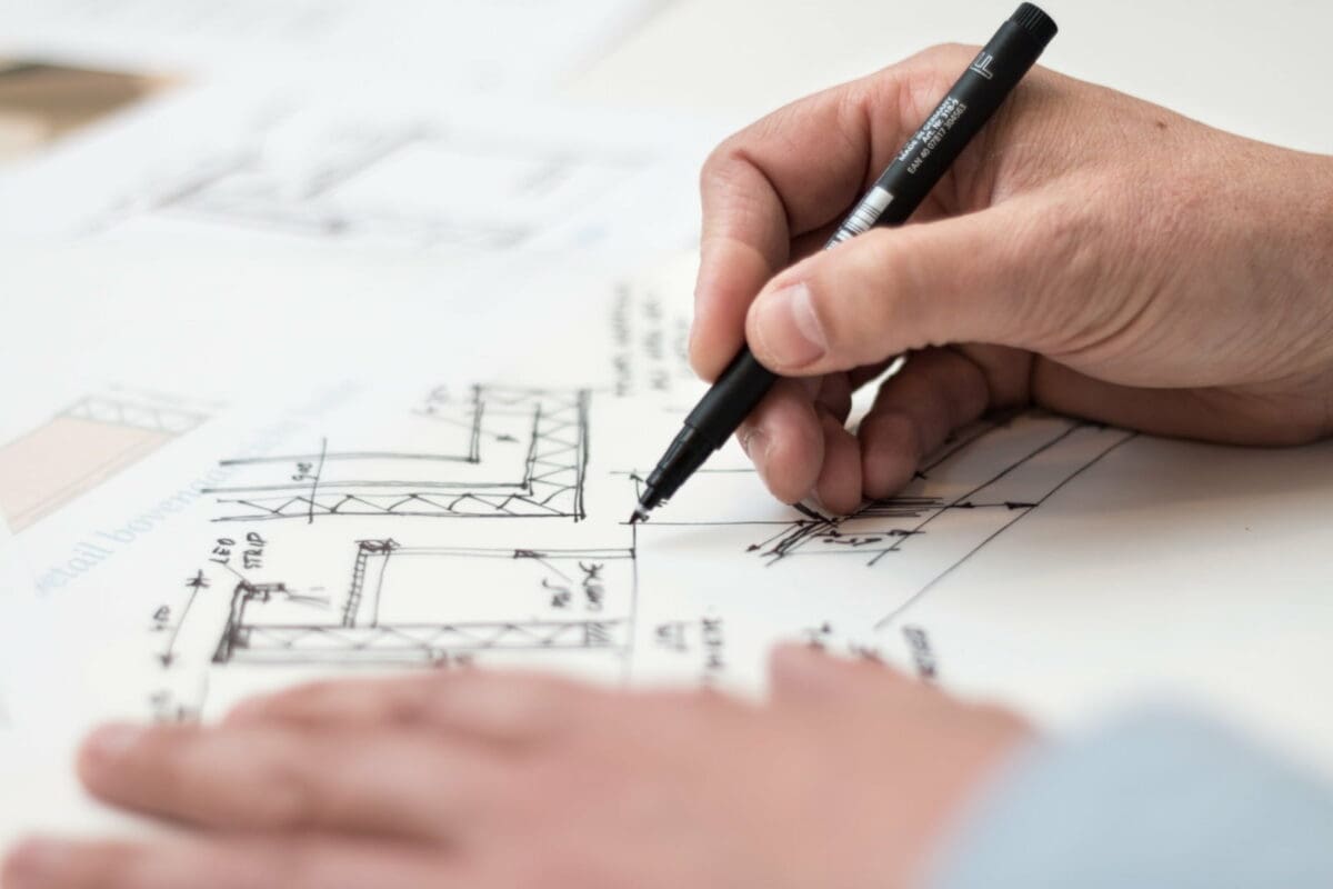 person-planning-office-technology-holding-black-pen-1109541 A person's hand skeching an office plan with a black pen.