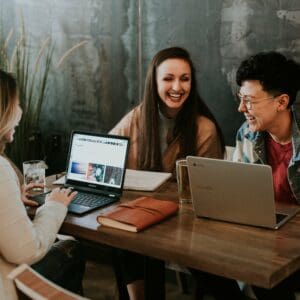 Three employees at a modern office working together on laptops, smiling and laughing, having a great employee experience through technology