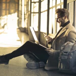 Man in a business suit sitting on the floor working on a laptop