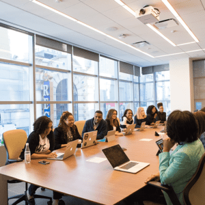 A full boardroom of people sitting in front of their Apple laptops