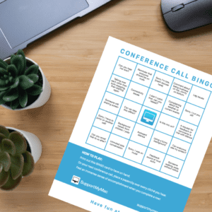 SupportMyMac's Conference Call Bingo card sitting on a wooden desk, in front of a laptop
