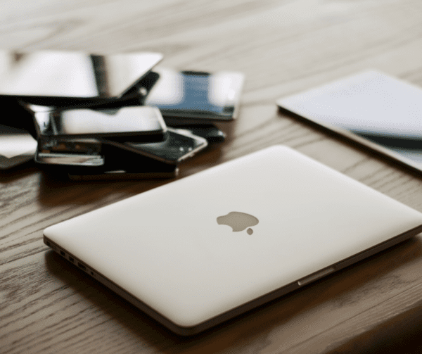 A pile of Apple devices sitting on a wooden table, including laptop, iPads and iPhones, for IT asset management